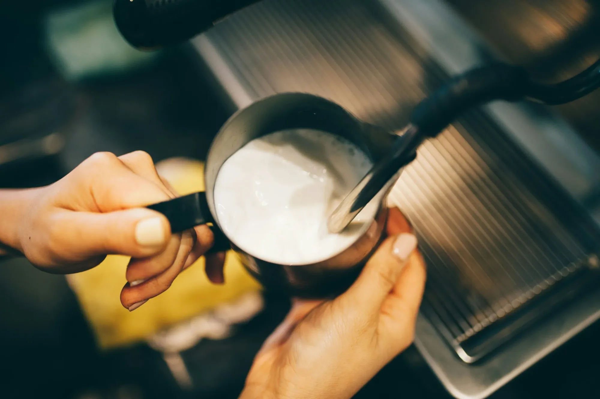 hands holding a metal pitcher of milk using a steam wand